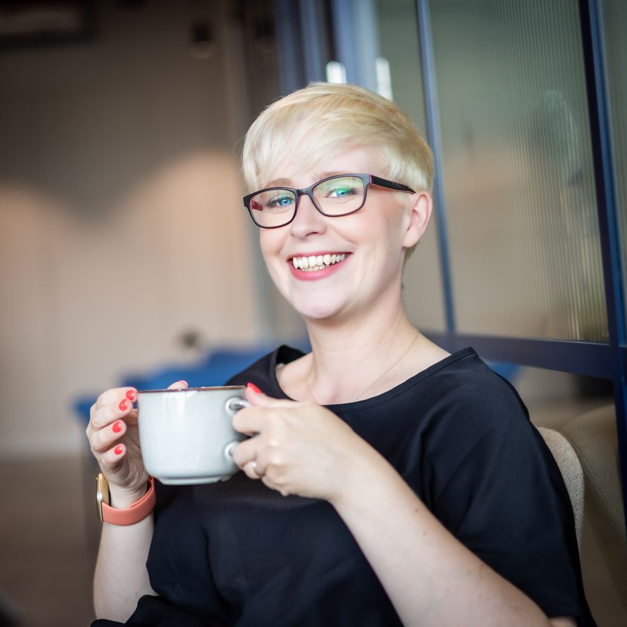 Jenny Lucas laughing, holding a white mug in both hands